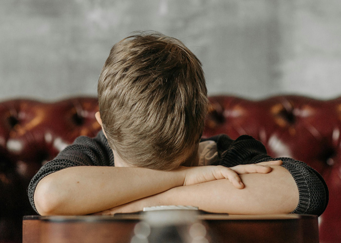 Upset boy hiding face on arms on leather couch
