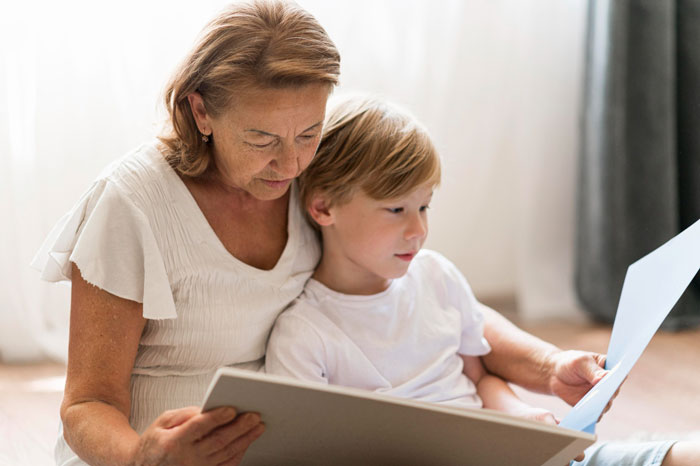 A grandmother and her grandchild read a book together, representing the family dynamics explored when a child is baptized.