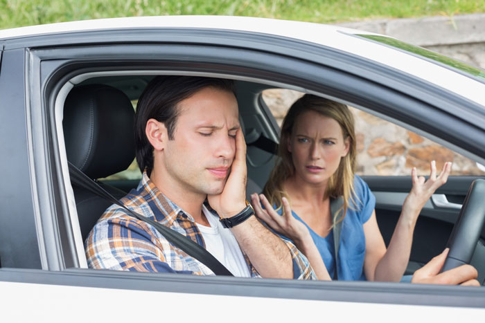 A frustrated man and an angry woman in a car, depicting a couple's dispute over a child's baptism and a dad's meltdown.