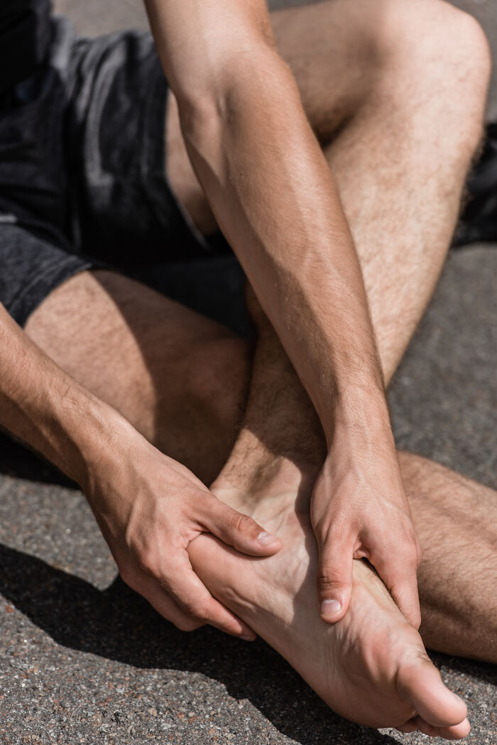 A man sits, clutching his bare foot in pain, illustrating the importance of routine cancer screening and health warning signs.
