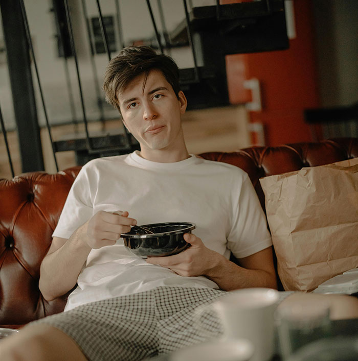 Man sitting on couch eating, reflecting on ugly cheating stories