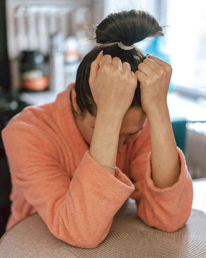 Stressed woman in orange robe covering face upset about cheating truth
