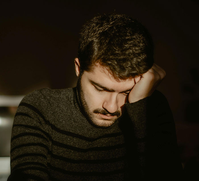 Sad man resting head on hand in dark room reflecting ugly cheating stories