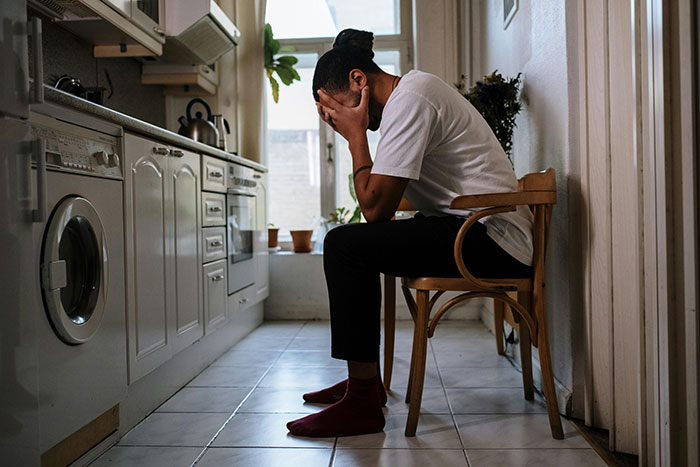 Man sitting in kitchen with head in hands depicting heartbreak from cheating stories