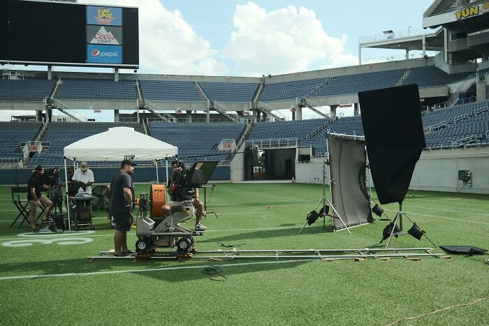 Film crew setting up equipment on a stadium field. This represents the costs of being related to a celebrity.