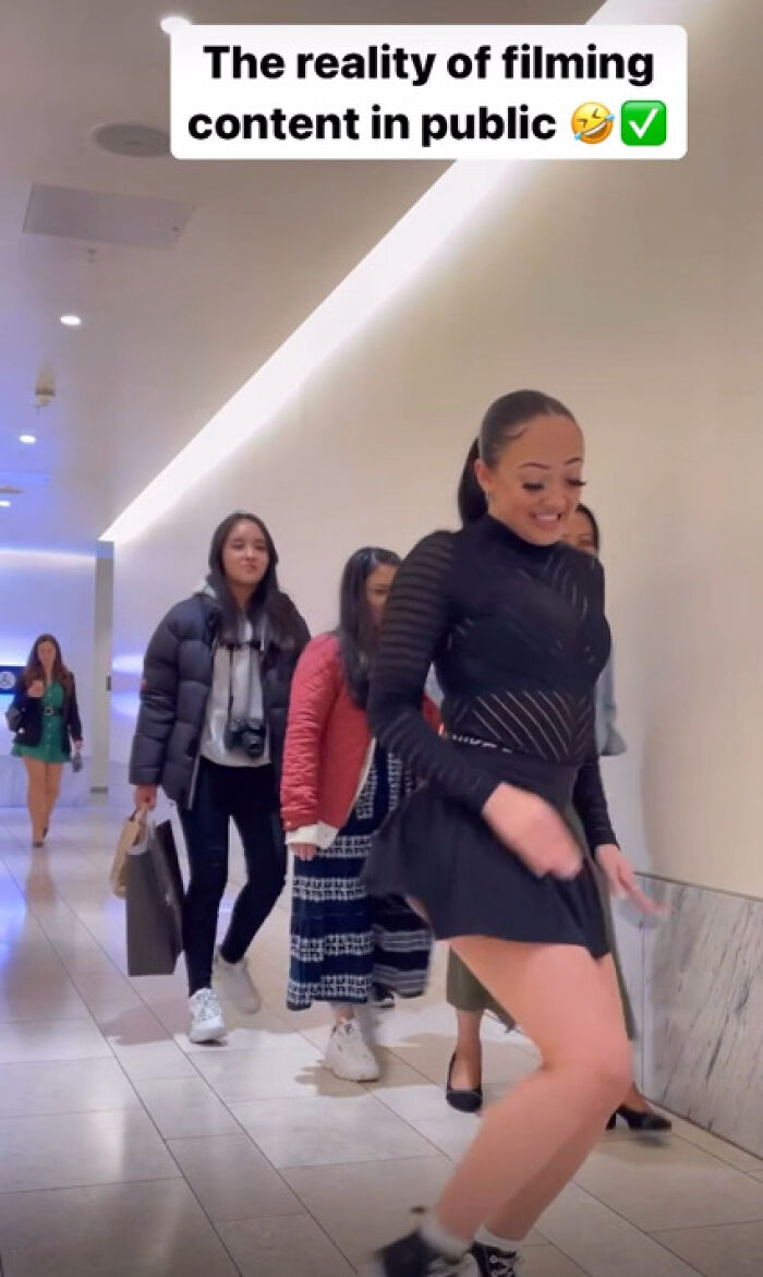 Woman filming content in public mall with people walking behind
