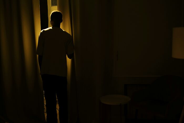 Silhouetted figure opening curtains into dark room at night