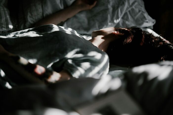 Person lying in bed asleep under soft lighting in a dark room