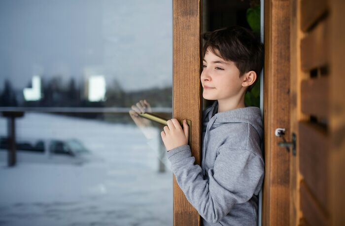 Boy opening door cautiously looking outside scared staying home alone
