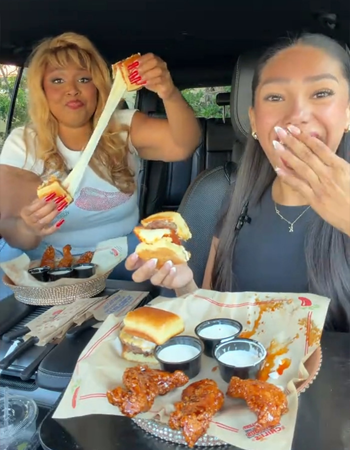 Lizzo and friend eating chicken wings and sliders in a car Lizzo and friend eating chicken wings and sliders in a car