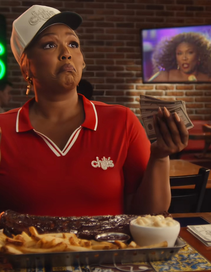 Lizzo in Chilis uniform holding cash with ribs and fries at table Lizzo in Chilis uniform holding cash with ribs and fries at table