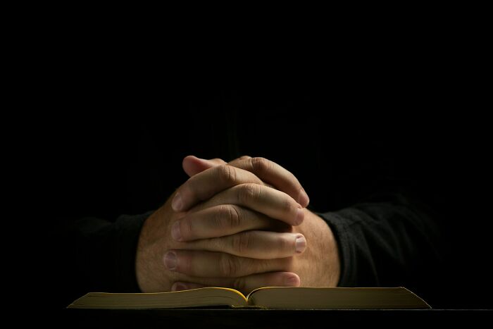 Praying hands resting on an open book, symbolizing reflection and stories that stay with you. Crossing to the other side.