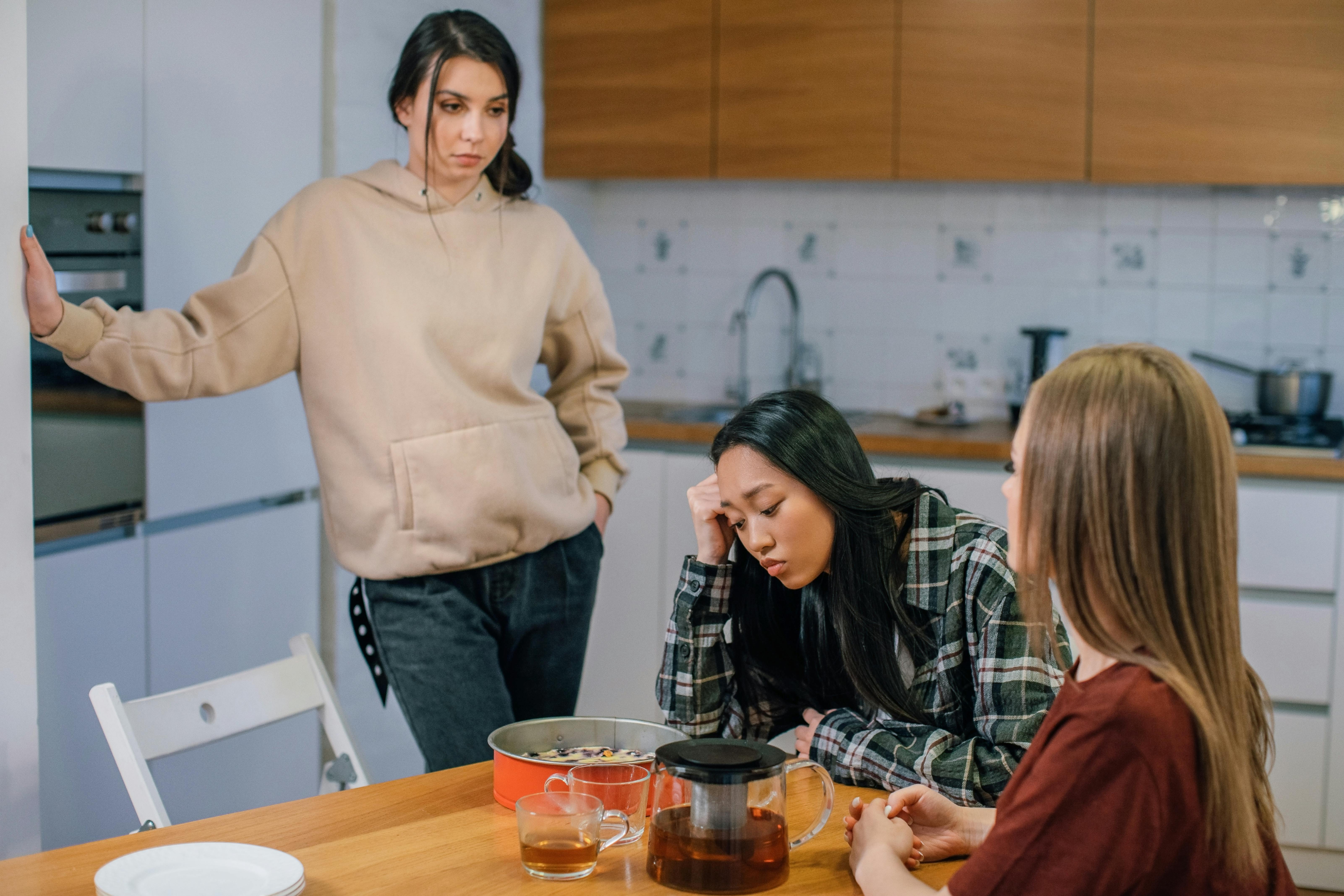 Woman looks upset while discussing bridesmaid choice with friends in kitchen Woman looks upset while discussing bridesmaid choice with friends in kitchen