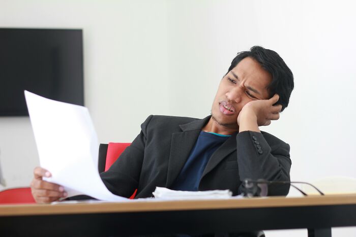 Tired man reading documents at office desk showing frustration and choosing peace over paycheck
