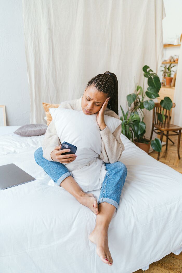 Woman looks upset hugging pillow while checking phone showing exes unhinged posts