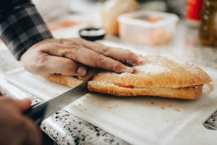 Hand cutting sandwich on white cutting board in kitchen setting
