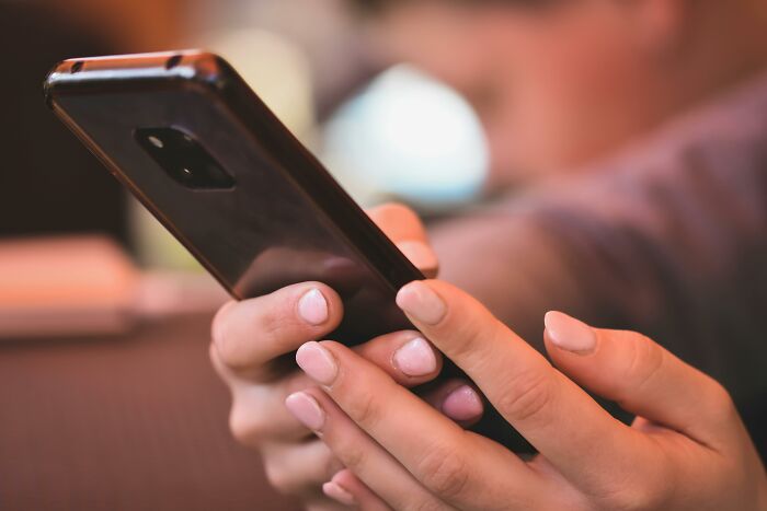 Close-up of hands with light pink nail polish scrolling on a dark smartphone. Discovering a hidden folder might mean your partner is cheating.