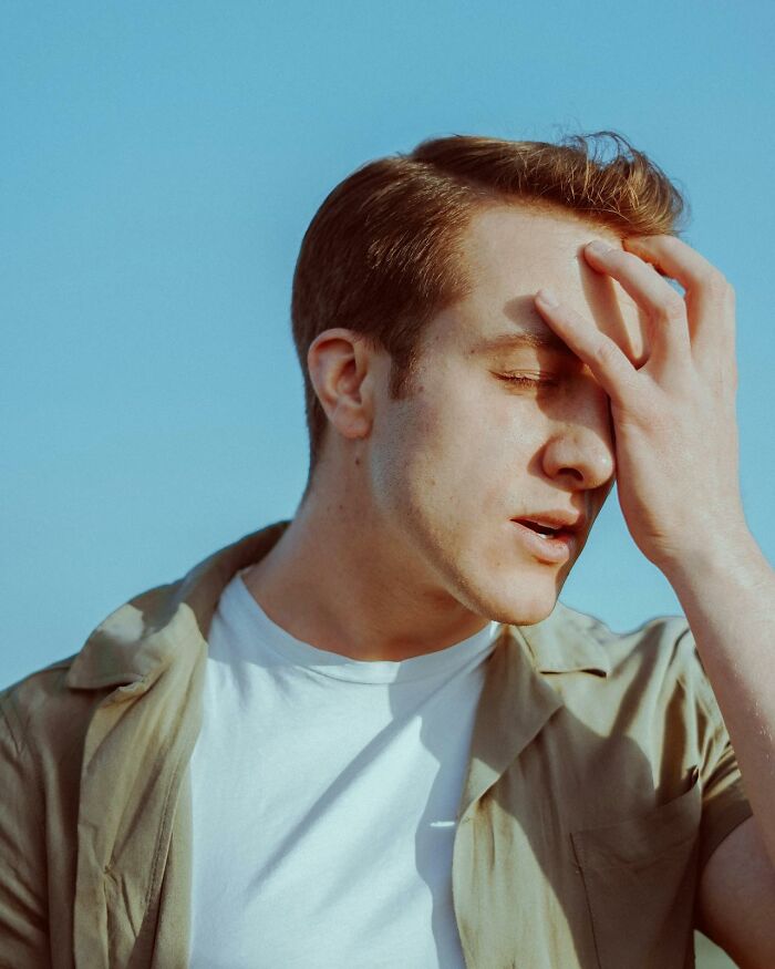 Man facepalming in frustration under clear blue sky