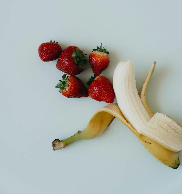 Peeled banana with strawberries on a white surface