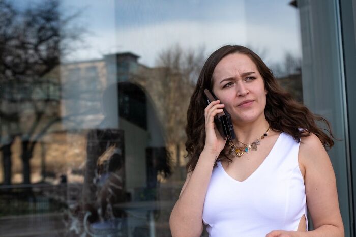 Woman in white talking on phone near glass wall looking concerned