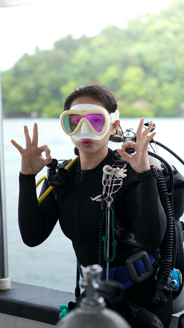 Scuba diver wearing gear and goggles making okay hand signs near water