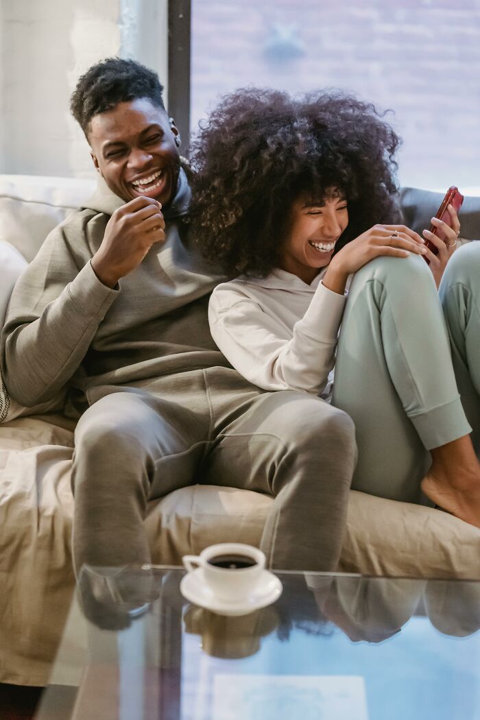 Couple laughing on couch with smartphone, highlighting fun and laughter among long term partners