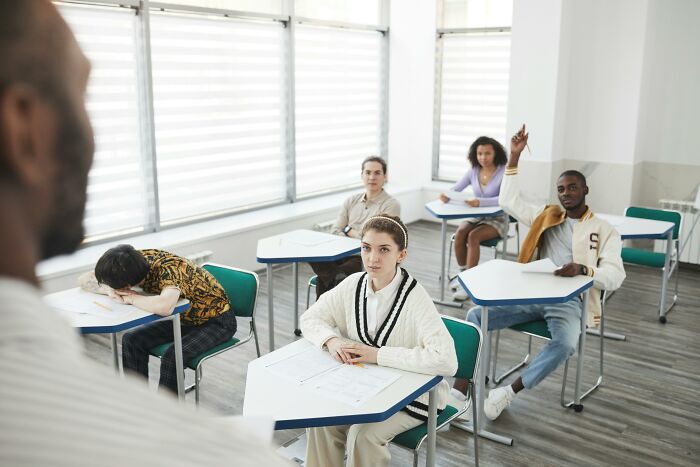 Students taking a 26-question school quiz in a classroom with one student raising a hand