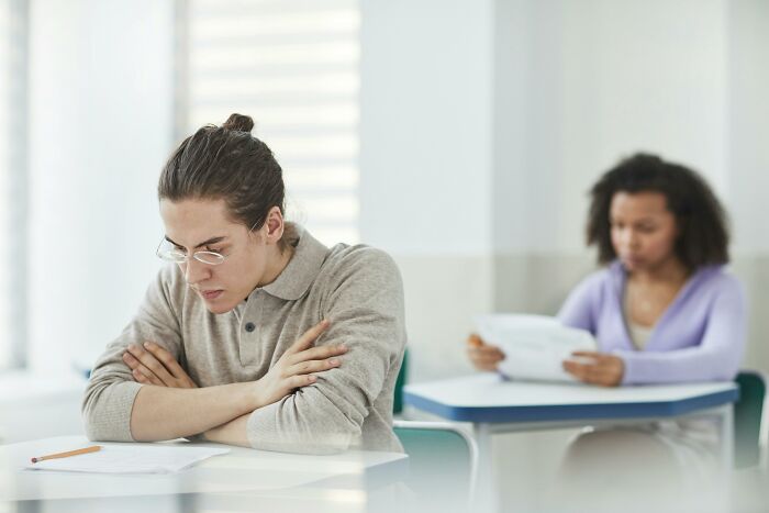 Young man concentrating during test in classroom with student behind