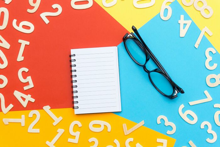 Notebook, eyeglasses, and scattered wooden numbers on colorful background for math puzzles and logic skills Notebook, eyeglasses, and scattered wooden numbers on colorful background for math puzzles and logic skills