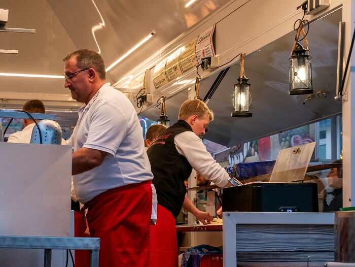 Workers preparing food in a brightly lit food truck at night, demonstrating aspects of privilege.