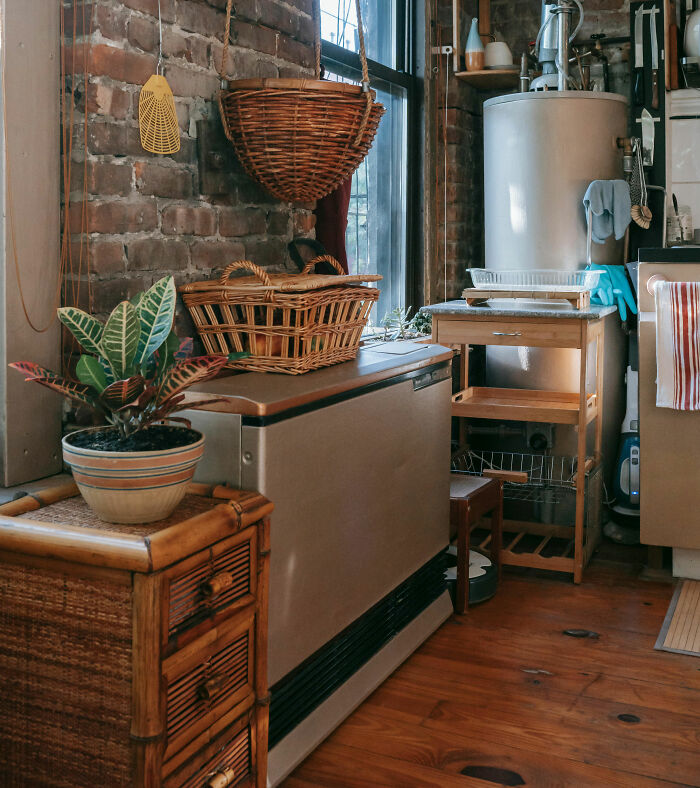 A rustic kitchen with a brick wall, potted plant, and woven baskets. Small changes can save you money.
