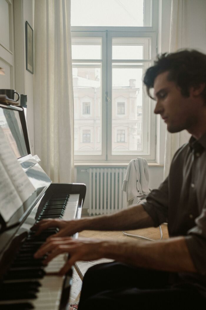 Man playing piano near window in softly lit room