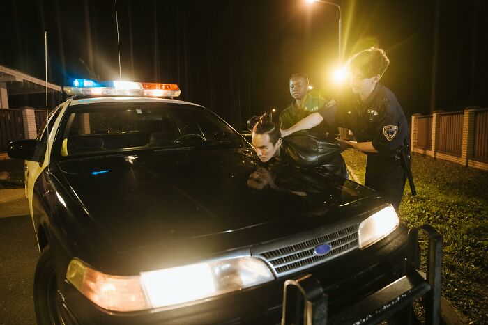 Two police officers detain a man over a patrol car at night, a scene of impossible cases for lawyers.