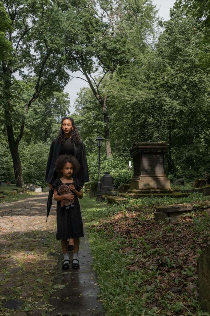 Mother and child dressed in black walk through cemetery path