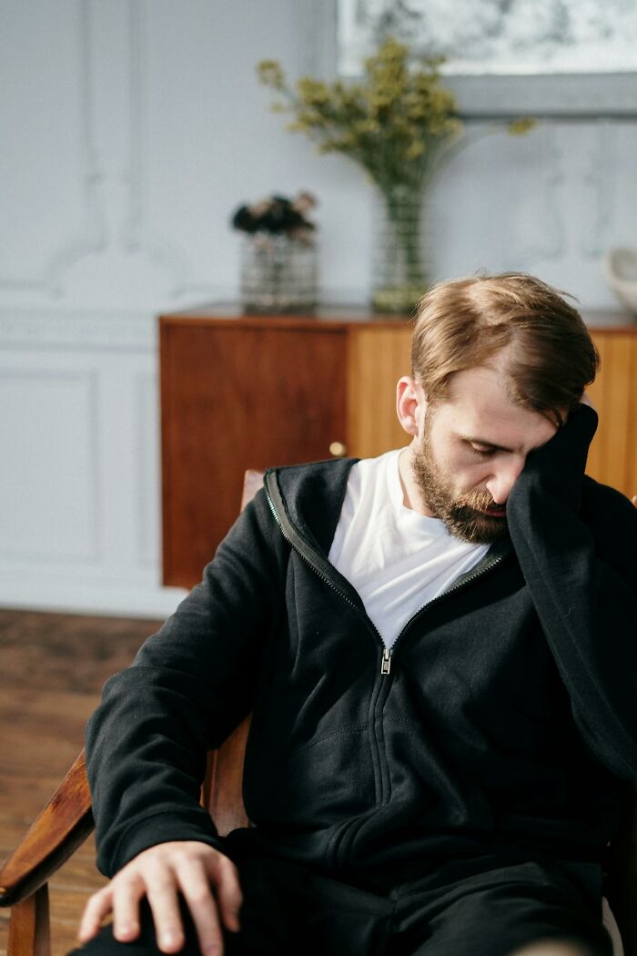 A man with a beard, wearing a black hoodie and white shirt, looks distressed with his hand on his face. This image reflects deeply immoral acts.