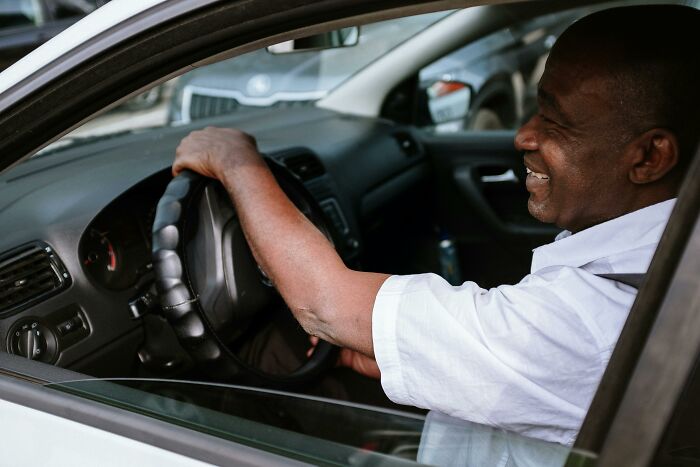 Smiling man sitting in parked car holding steering wheel
