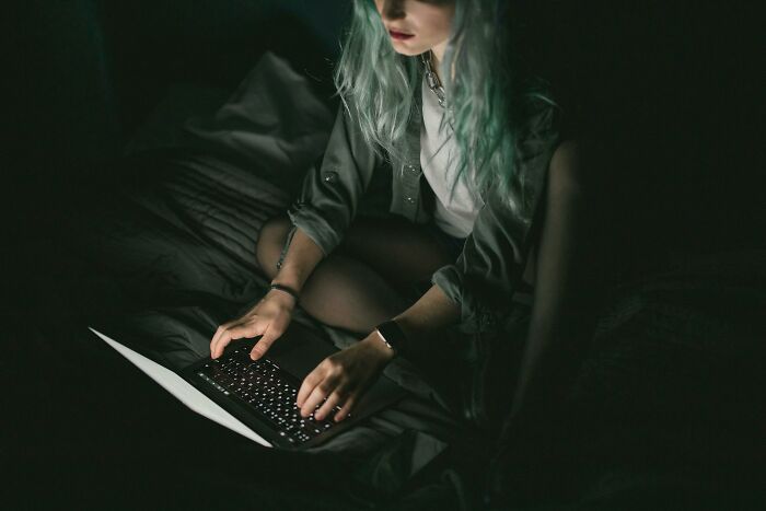 Woman with green hair typing on laptop in dark room with low light