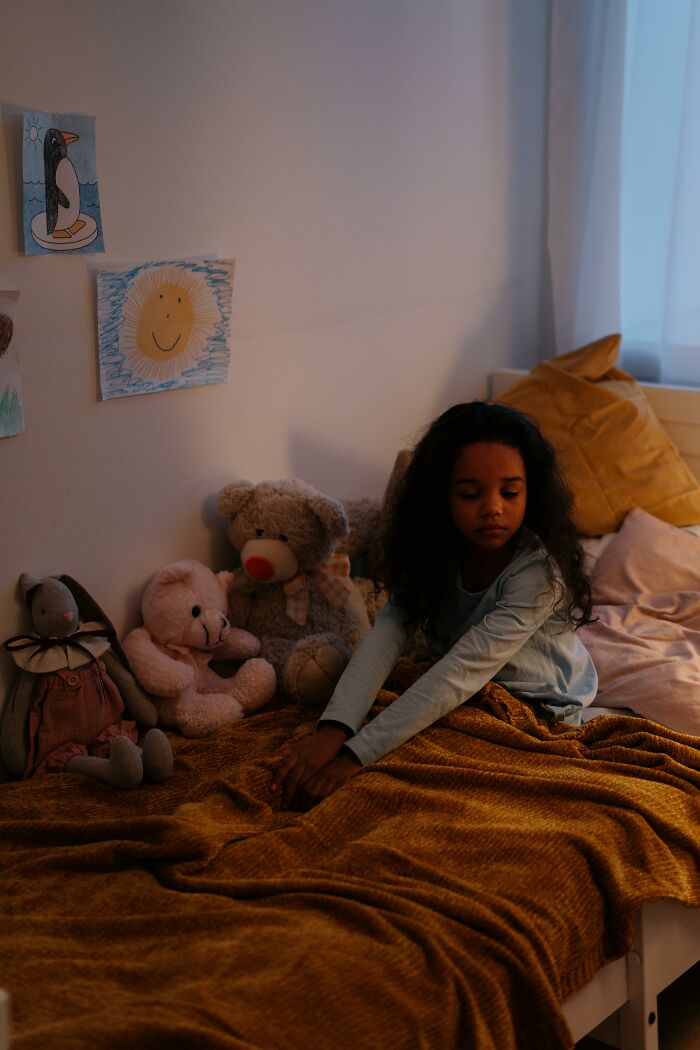 Child sitting on bed with teddy bears in dimly lit room