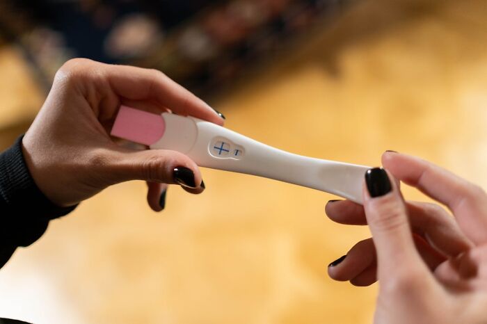 Hands holding positive pregnancy test with plus sign
