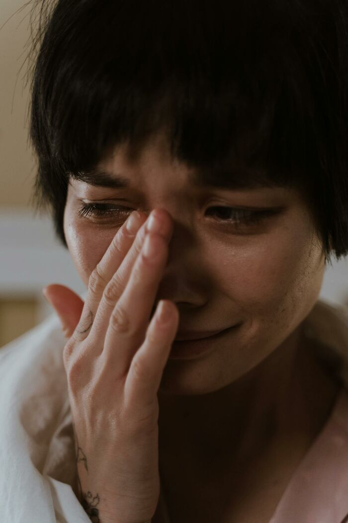 A person with short dark hair wiping away tears from their eyes. This image evokes questioning reality and glitches.