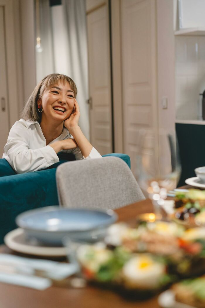 A woman laughing at a dinner table, enjoying tales of wedding drama stories.