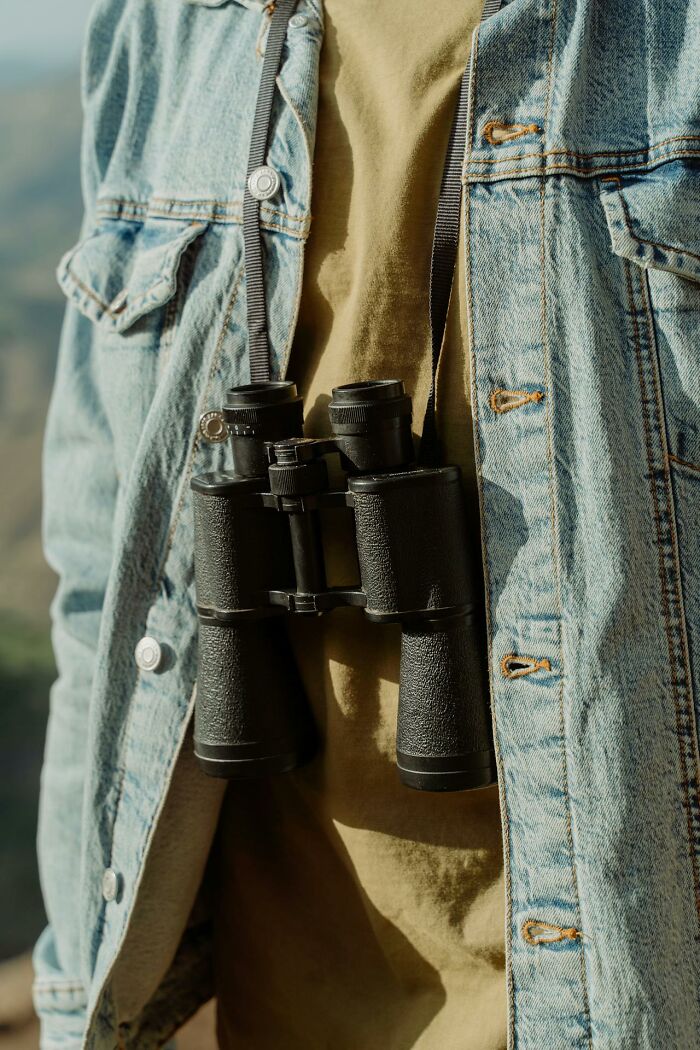 Close-up of binoculars hanging from denim jacket outdoors