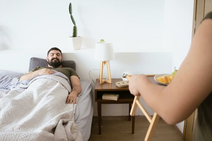 Man resting in bed while someone brings breakfast tray in quiet room