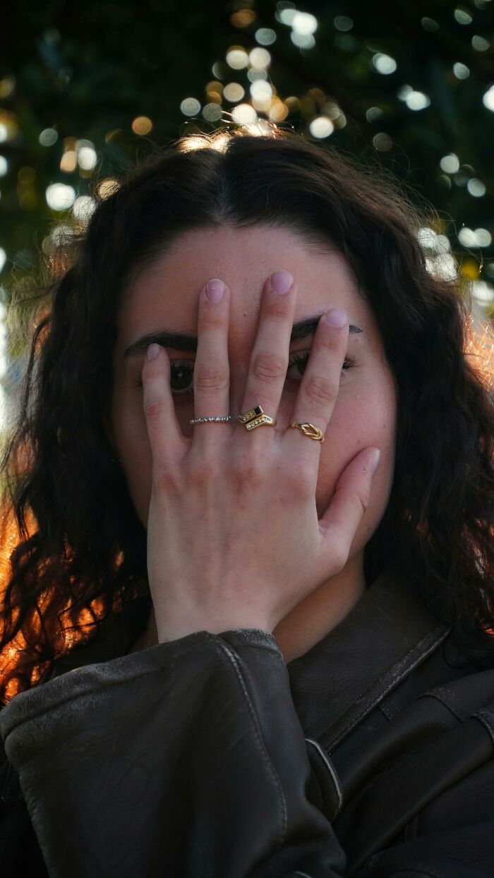 A woman covering her face with her hand, wearing rings, with light filtering through her hair. Glitches in the matrix.
