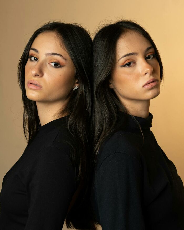 Portrait of serious twin women standing back to back