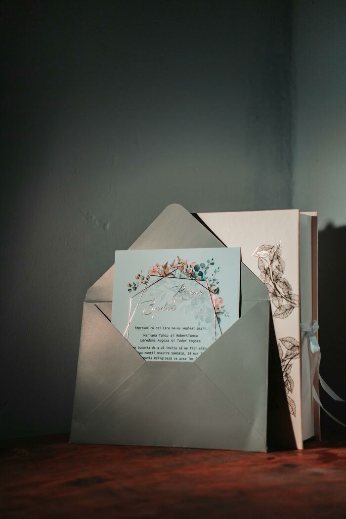 An elegant wedding invitation with floral accents, partially in a grey envelope, next to a decorative box for wedding memories.