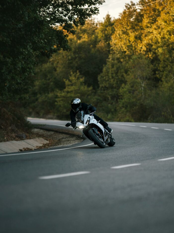 A motorcyclist leans into a turn on a winding road with trees in the background, very creepy things in nature.