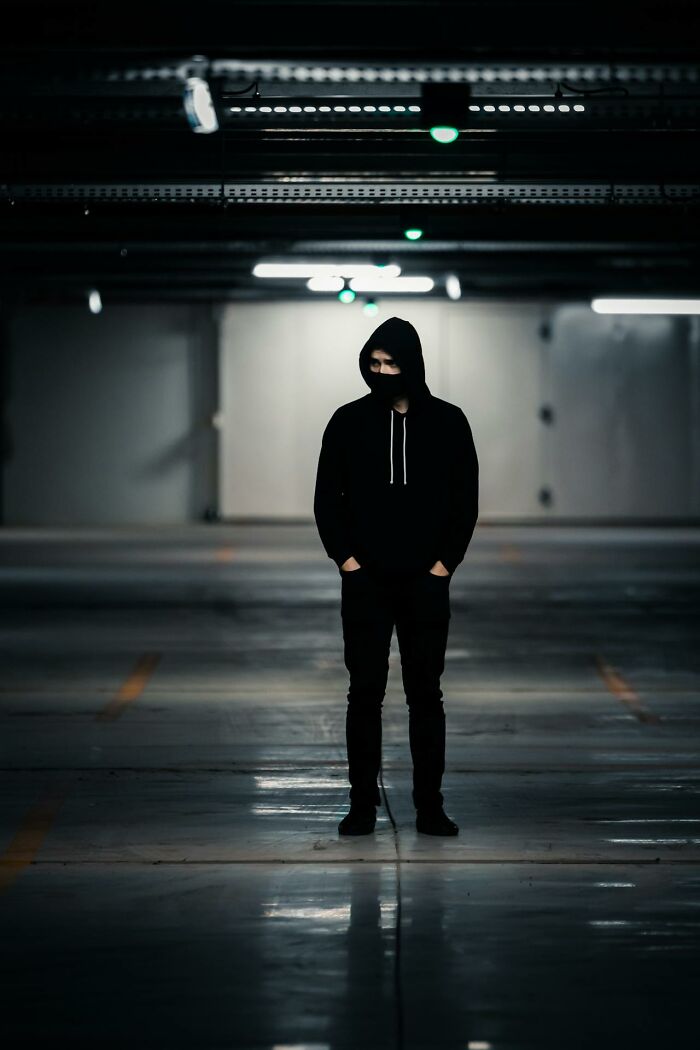 Person in dark hoodie standing alone in a dimly lit parking garage
