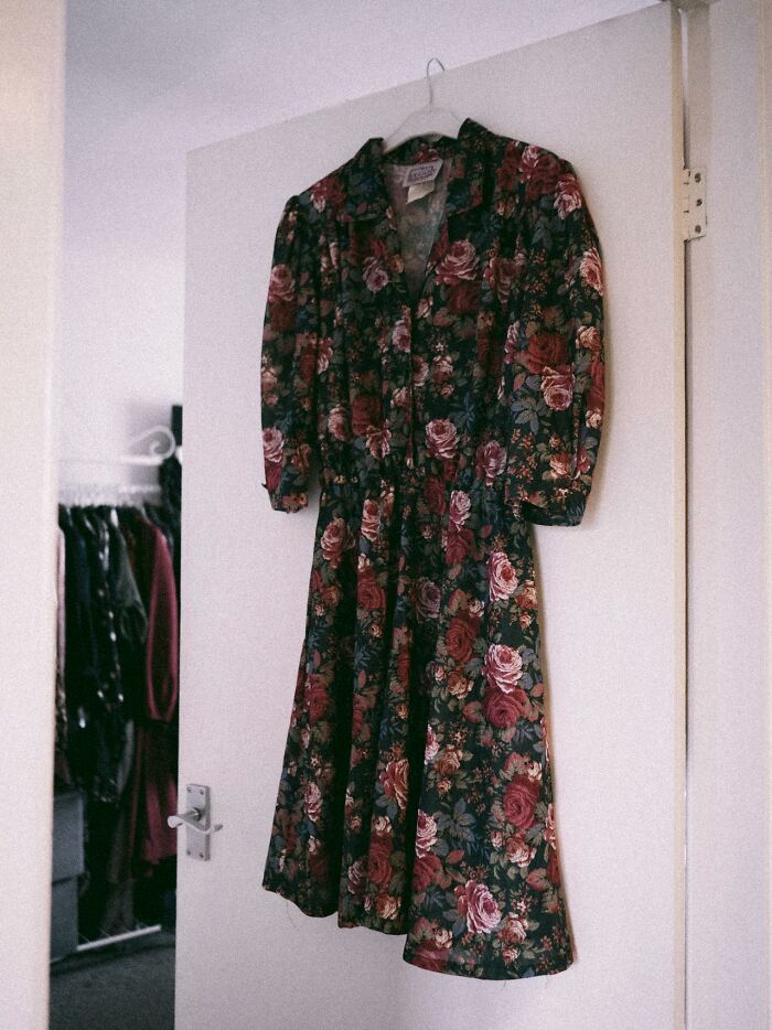 A floral dress with red and pink roses hangs on a white door. A glimpse into a closet questions reality.