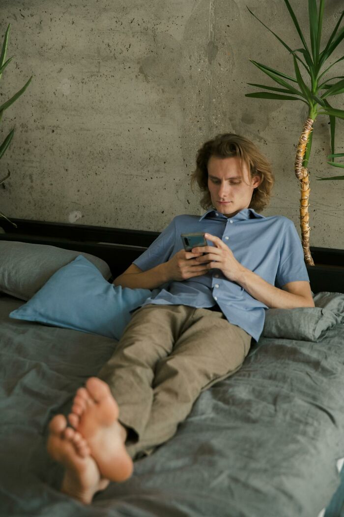 Young man lounging on bed using phone showing lazy time avoiding trouble